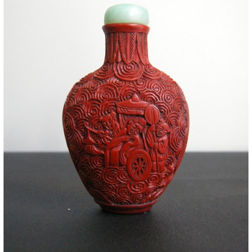 Cinnabar lacque snuff bottle on metal decorated and sculpted with a rider on one side and characters on a trolley on the other